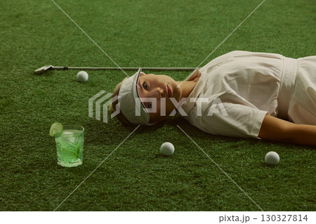 Woman golfer lying on grass with lime cocktail golf balls and club serene expression 130327814