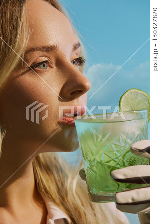 Close up of woman drinking cocktail with lime wearing golf glove under blue sky relaxed expression Close up of woman drinking cocktail with lime wearing golf glove under blue sky relaxed expression 130327820