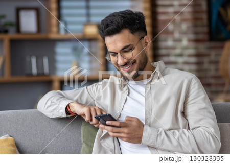 Smiling man using smartphone on couch, enjoying leisure time at home. Captures joy, connectivity, and relaxation with modern technology. Perfect representation of digital lifestyle 130328335