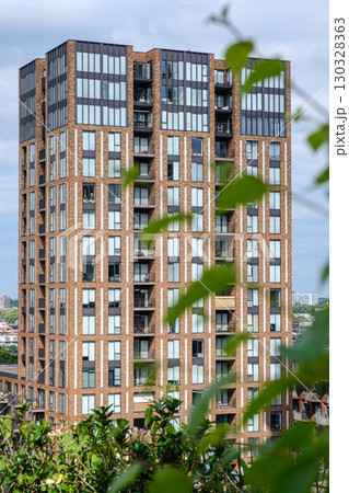 Modern residential building with brick facade and large windows, surrounded by greenery 130328363