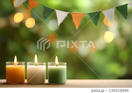 Three candles in saffron, white, and green colors are placed on a wooden surface. A festive bunting with the same colors hangs above, creating a celebratory atmosphere. India, Indian Independence Day. 130328994