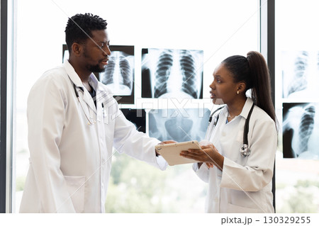 Male and female doctors communicating in medical setting with x-rays displayed near window indoors 130329255