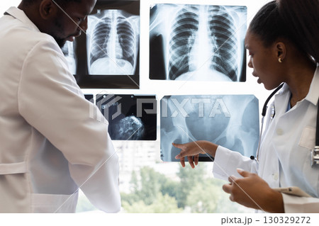 Male and female doctors analyzing x-ray results near clinic window during consultation. They review patient diagnostics to determine findings and treatment options for optimal healthcare solutions. 130329272