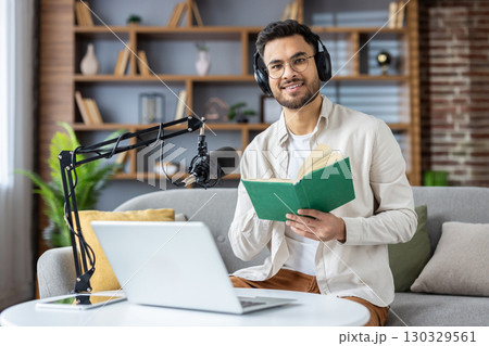 Man wearing headphones while recording podcast at home. Engaged in content creation using professional microphone and laptop. Holding book, showcasing knowledge sharing and modern communication. Man wearing headphones while recording podcast at home. Engaged in content creation using professional microphone and laptop. Holding book, showcasing knowledge sharing and modern communication. 130329561