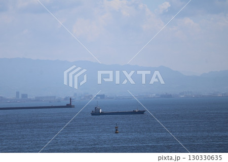 青い海面の海と大型タンカーと灯台のある突堤と霞む街と山と雲と青空の風景 青い海面の海と大型タンカーと灯台のある突堤と霞む街と山と雲と青空の風景 130330635