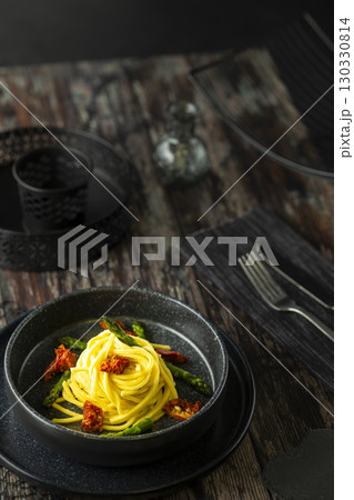 Delicious spaghetti with asparagus and dried tomatoes resting on a black plate 130330814