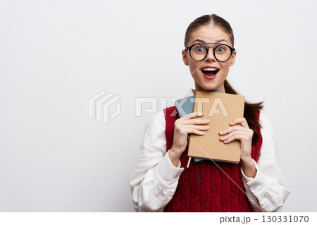 Cheerful young woman holding books in front of a neutral white background, expressing excitement and joy while wearing glasses Concept of education, learning, and reading Cheerful young woman holding books in front of a neutral white background, expressing excitement and joy while wearing glasses Concept of education, learning, and reading 130331070