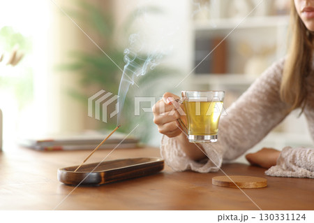 Woman hand holding tea cup beside incense stick burning 130331124