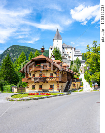 Mauterndorf Castle stands majestically against the backdrop of the Austrian Alps. A charming wooden building features colorful flowers, showcasing the region's beauty and rich history. 130331238