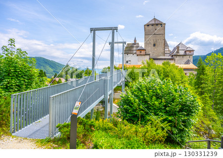 Mauterndorf Castle stands prominently in Austria, surrounded by lush greenery and scenic mountains. Visitors can access it via a modern bridge leading to its historic grounds. 130331239