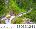 Johannes Waterfall cascades down rocky terrain surrounded by lush greenery in Obertauern, Austria. Hikers enjoy the natural beauty and serene atmosphere of the alpine landscape. 130331241