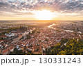 Sunrise casts a warm glow over Prague Castle and the vibrant rooftops of the city. The picturesque landscape, with rivers and greenery, captures a serene morning atmosphere in Praha. 130331243