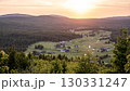 As the sun sets over Jizerka Village in the Jizera Mountains, the landscape glows with warm hues. The peaceful village rests amidst rolling hills and dense forests, evoking a sense of calm. 130331247