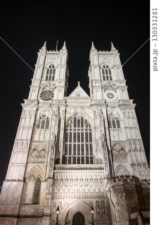 Westminster Abbey stands majestically under the night sky, showcasing its gothic architecture. The illuminated facade highlights intricate details, captivating visitors in London, England. 130331281