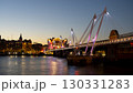 The illuminated Charing Cross Bridge spans the River Thames in London during twilight. Surrounding lights reflect on the water, creating a peaceful evening atmosphere for viewers. 130331283
