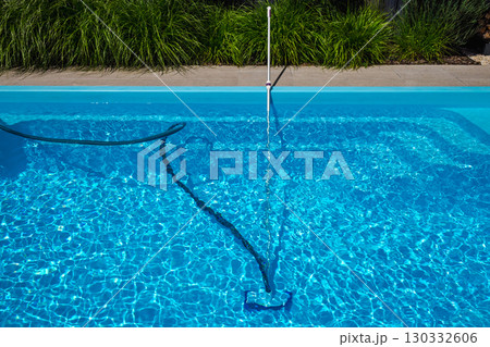 Telescopic pool vacuum and hose cleaning the clear blue bottom of a swimming pool, used for manual maintenance under sunny summer conditions. Telescopic pool vacuum and hose cleaning the clear blue bottom of a swimming pool, used for manual maintenance under sunny summer conditions. 130332606