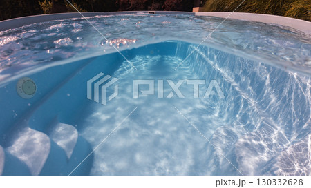 Underwater and above view of a clear blue swimming pool with curved steps and sunlight reflections on the floor and walls, evoking calm and leisure. Underwater and above view of a clear blue swimming pool with curved steps and sunlight reflections on the floor and walls, evoking calm and leisure. 130332628