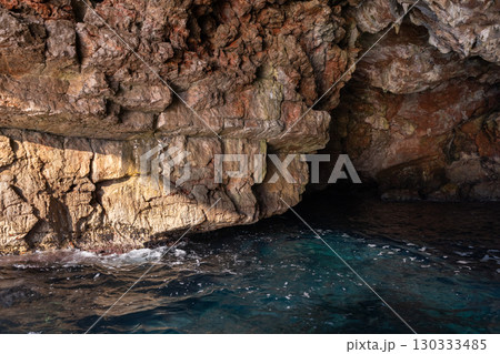 A scenic view of a rocky coastal cave entrance with clear blue water 130333485