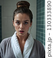 Woman in bathrobe in the bathroom looks at camera with surprised expression on her face 130333890