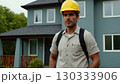 Man in yellow helmet standing in front of the house. He's wearing uniform and he's construction 130333906