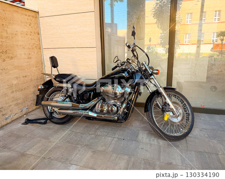 Black motorcycle parked by a building. Transportation, lifestyle, and freedom on two wheels in city life. Black motorcycle parked by a building. Transportation, lifestyle, and freedom on two wheels in city life. 130334190