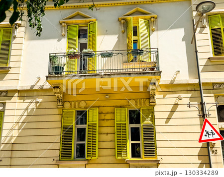 Historic building facade with yellow window shutters and balcony railing. Architectural detail symbolizing heritage, urban culture and European cityscape. Historic building facade with yellow window shutters and balcony railing. Architectural detail symbolizing heritage, urban culture and European cityscape. 130334289
