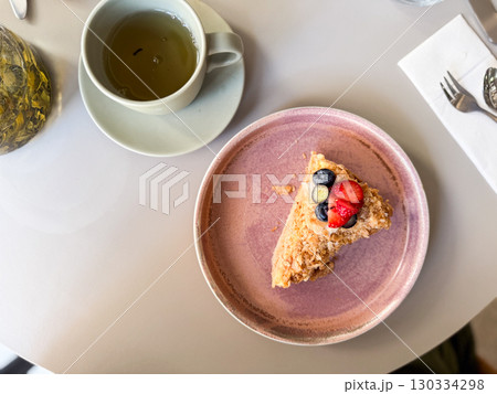 Overhead view of cake slice with fresh berries and tea cup on table. Sweet dessert symbolizing indulgence, lifestyle dining and gourmet culture. Overhead view of cake slice with fresh berries and tea cup on table. Sweet dessert symbolizing indulgence, lifestyle dining and gourmet culture. 130334298