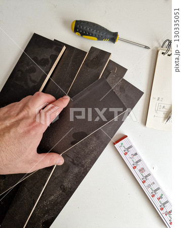 Hand Holding Wooden Plank with Measuring Tape and Sandpaper in Workshop 130335051