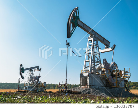 Oil pumps operate in a vast field under a clear blue sky at midday in rural area Oil pumps operate in a vast field under a clear blue sky at midday in rural area 130335707
