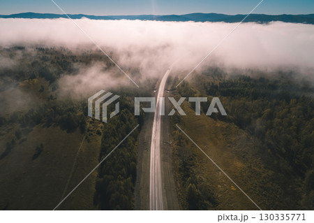 Scenic drive through fog-covered landscape in early morning light, showcasing a winding highway and lush terrain Scenic drive through fog-covered landscape in early morning light, showcasing a winding highway and lush terrain 130335771