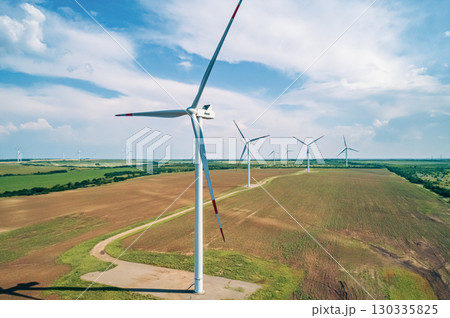 A row of large wind turbines stands tall in a vast, open field, showcasing renewable energy production. A row of large wind turbines stands tall in a vast, open field, showcasing renewable energy production. 130335825