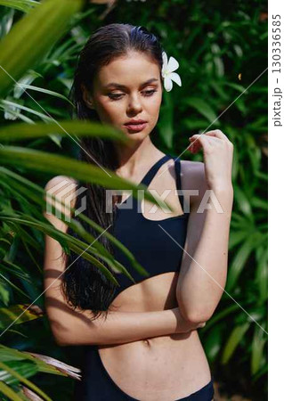 Tropical Vacation Paradise Woman in Black Bikini Top with Flower in Hair Standing in Front of Palm Trees 130336585