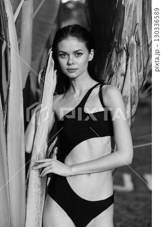 Elegant woman in a classic black swimsuit posing gracefully for a black and white photo shoot by the pool 130336589