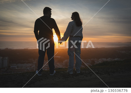 Couple holding hands watching amazing sunset over city and coastline 130336776