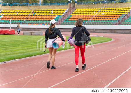 Two young women in activewear carrying yoga mats walk through a stadium Two young women in activewear carrying yoga mats walk through a stadium 130337003
