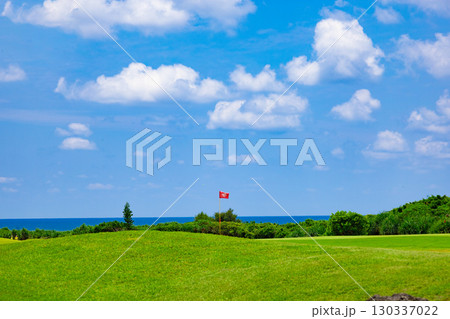 爽やかな南国の青空と青い海が映えるリゾートのゴルフ場とグリーンの旗（沖縄県宮古島市） 130337022