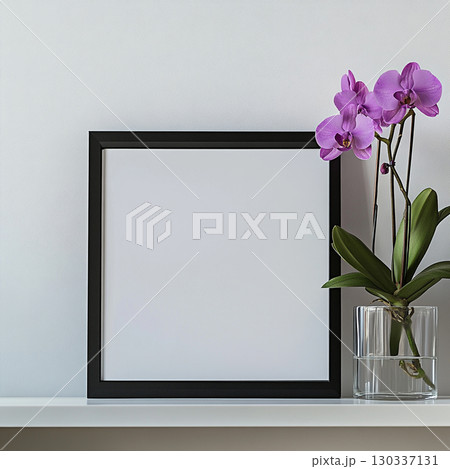 A simple, clean shot of a black-framed blank poster on a white shelf next to a vibrant purple orchid in a clear vase. It's a minimalist scene. 130337131
