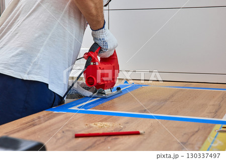 repairman using handheld electric jigsaw and cutting hole for the sink in the kitchen countertops, Woodworking and carpentry concept 130337497