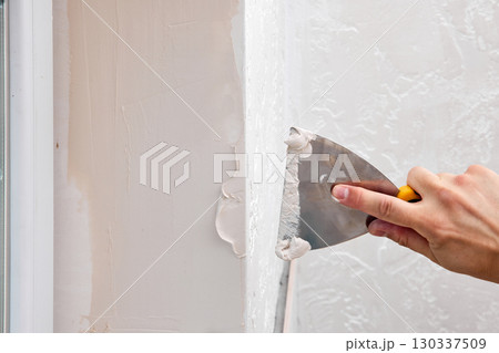 Caucasian plasterer man with a spatula applying finishing putty on a window opening Caucasian plasterer man with a spatula applying finishing putty on a window opening 130337509