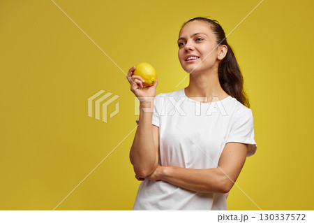 happy Caucasian woman holds fresh lemon on yellow background, vitamin fruit diet 130337572