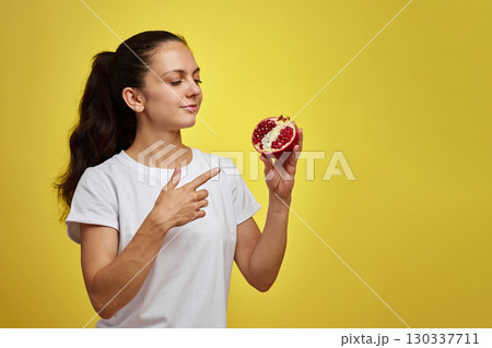 Beautiful happy woman holding pomegranate on yellow background 130337711