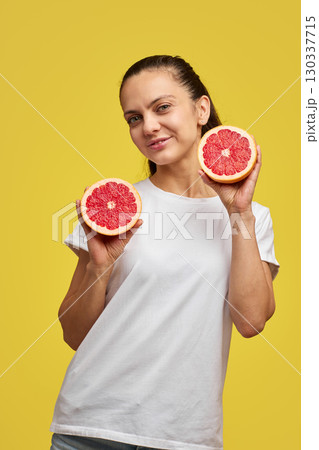 Happy Caucasian woman holds grapefruit halves on yellow background 130337715