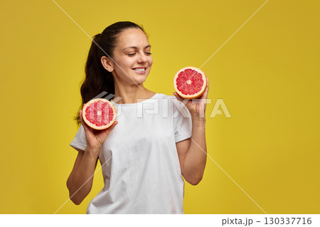 Happy Caucasian woman holds grapefruit halves on yellow background 130337716