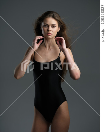 young woman in black swimsuit posing confidently on gray background with natural makeup and loose hair young woman in black swimsuit posing confidently on gray background with natural makeup and loose hair 130338827
