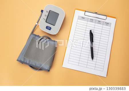 Blood pressure monitor with a data recording pad and pen is placed on the table, showing that it is a practice of self care by recording daily health data. Blood pressure monitor with a data recording pad and pen is placed on the table, showing that it is a practice of self care by recording daily health data. 130339883