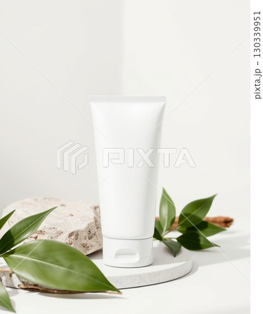 A white cosmetic tube with a minimalistic design on a stone and leaves. 130339951