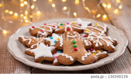 Christmas gingerbread cookies with icing and colorful candy decorations arranged on a plate with festive lights in the background 130340139