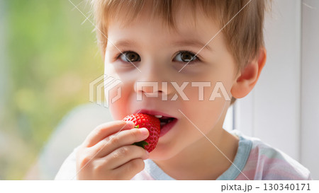 Cute young boy eating fresh strawberry near window in natural daylight. Sweet and healthy childhood moment. 130340171