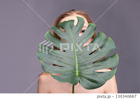 Young caucasian female partially covered by monstera leaf on neutral background 130340667