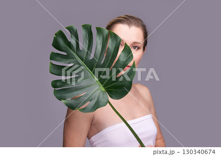 Caucasian adult female partially hidden behind large monstera leaf on gray Caucasian adult female partially hidden behind large monstera leaf on gray 130340674